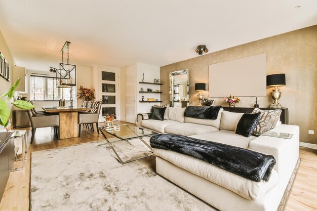 Modern open-concept living and dining room with a large beige sectional sofa, glass coffee table, wooden dining table, and elegant decor in neutral tones.