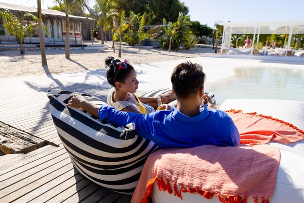 A couple relaxing by a beachside pool on bean bags, enjoying drinks under the sun at a tropical resort getaway