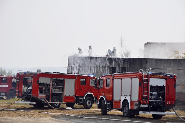 Fire trucks and firefighters spray water on a burning building during a fire emergency response operation.