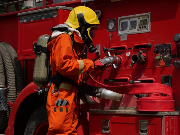 Firefighter in protective gear operates a fire truck hose system, preparing equipment during an emergency response.