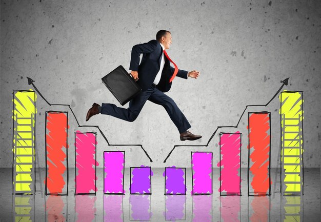 Businessman in a suit and red tie jumping over colorful hand-drawn bar graphs while holding a briefcase, symbolizing growth and success.