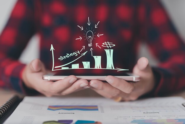 Person holding a smartphone with a digital growth chart, strategy text, and lightbulb icon displayed above it.