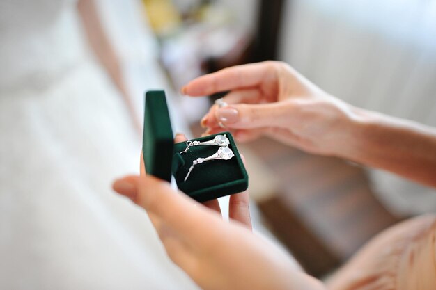 Hands opening a green jewelry box revealing elegant drop earrings inside.