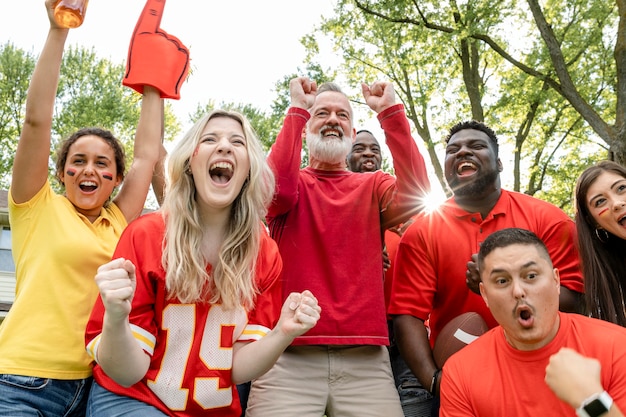 Group of excited sports fans in red cheering outdoors, raising fists and celebrating together.